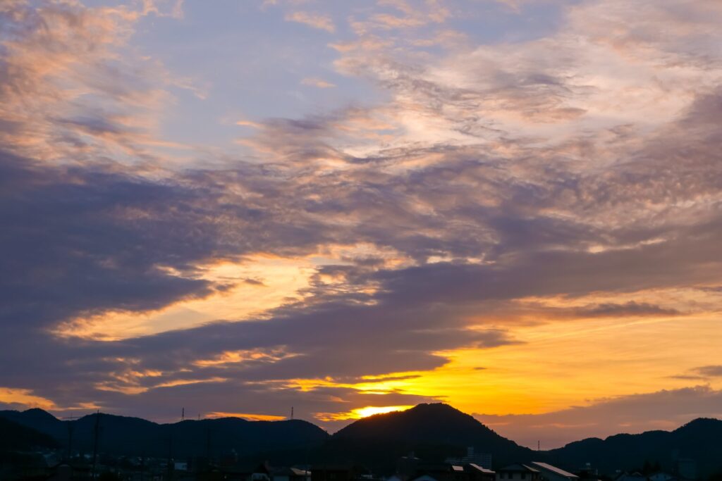 朝5時40分の朝焼けの作例。雲がオレンジと紫に染まり、山と住宅街がシルエットになっている