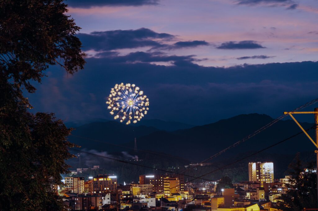 遠景の花火の作例。望遠90mmで、夕暮れの紫の空と街の灯りごと花火を切り取っている