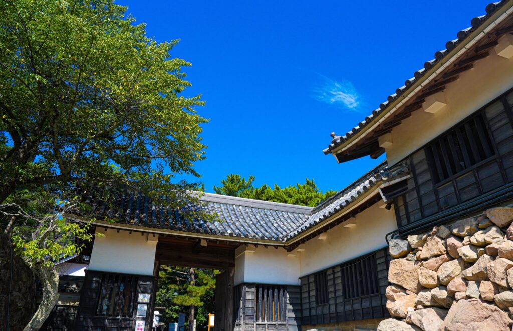 FE 24-70mm F2.8 GM IIを24mm・F8で撮影した作例。城の門と白壁・瓦屋根・石垣を見上げた構図で、青空まで隅々まで解像している